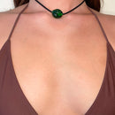 Made by a small family in Java. Worn as a choker, the emerald green glass pendant at the throat above a brown bikini top.