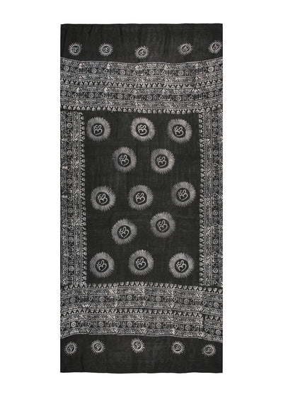 One piece of cloth, worn three ways. The black Midnight Om Sarong laid flat, white Om sunbursts and script borders on a cotton-rayon blend.